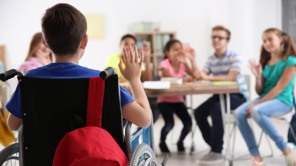 Boy in wheelchair waiving to a class of multicultural students